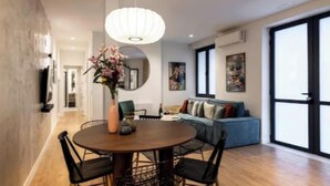 A modern living room with a round dining table, black chairs, a blue sofa, and a large window. - Luxury Renovated 3-Bedroom Apartment in the Heart of Madrid (Madrid)