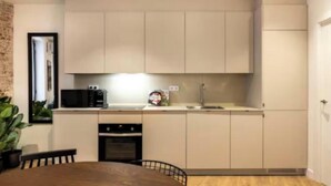 A compact kitchen with a microwave, oven, and sink. There is a dining table with chairs. - Luxury Renovated 3-Bedroom Apartment in the Heart of Madrid (Madrid)