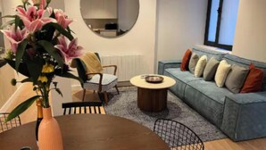 A modern living room with a round coffee table, a sofa with cushions, a chair, and a vase with flowers. - Luxury Renovated 3-Bedroom Apartment in the Heart of Madrid (Madrid)