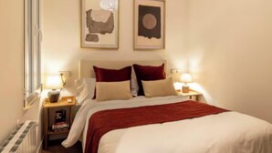A hotel room with a bed, two bedside lamps, a nightstand, a window, and two framed pictures on the wall. - Luxury Renovated 3-Bedroom Apartment in the Heart of Madrid (Madrid)