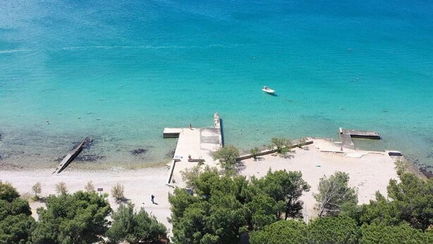 A beach with clear turquoise water, a boat, and a building with a dock. - Apartment Recreation apt 3 (Sibenik)