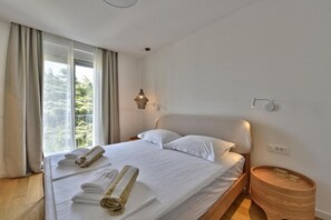 A hotel room with a large bed, a bedside table, a lamp, and a view of trees through the window. - Apartment Recreation Apt4 (Sibenik)