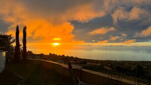 Vista al atardecer desde un balcón con vista a un cuerpo de agua y un pueblo lejano.