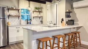 A modern kitchen with white cabinetry, a large island with bar stools, and a window with a view. - New! Pet Friendly Lake Nockamixon Cottage Hideaway (Quakertown)