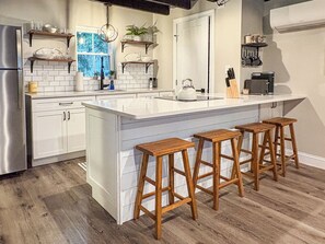 A modern kitchen with white cabinetry, a large island with bar stools, and a window with a view.