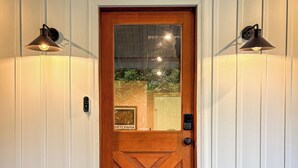A wooden door with a glass panel, a welcome mat, and two wall-mounted lights. - New! Pet Friendly Lake Nockamixon Cottage Hideaway (Quakertown)