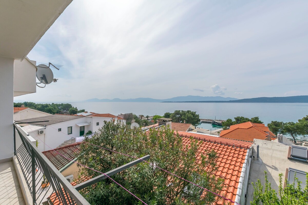 A balcony with a view of a coastal area, red-tiled roofs, and a body of water in the distance.