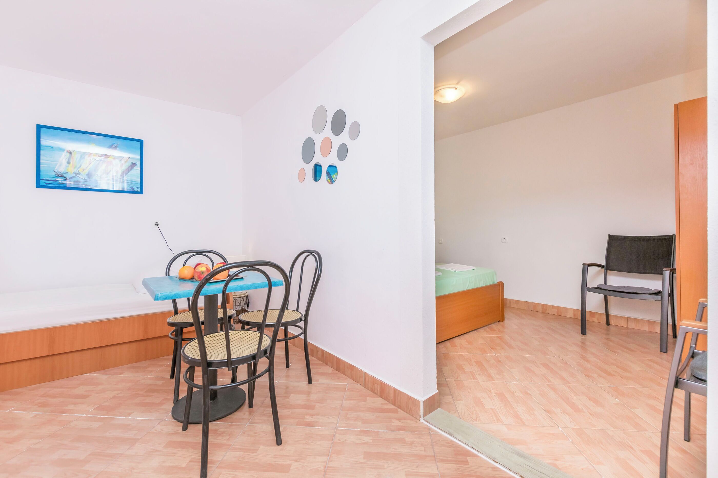 A room with a dining table, chairs, a bed, and a wall with a painting and decorative circles.