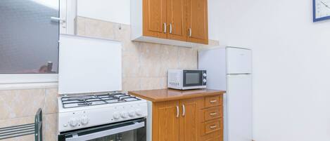 A kitchen with wooden cabinets, a microwave, a refrigerator, a gas stove, and an oven.
