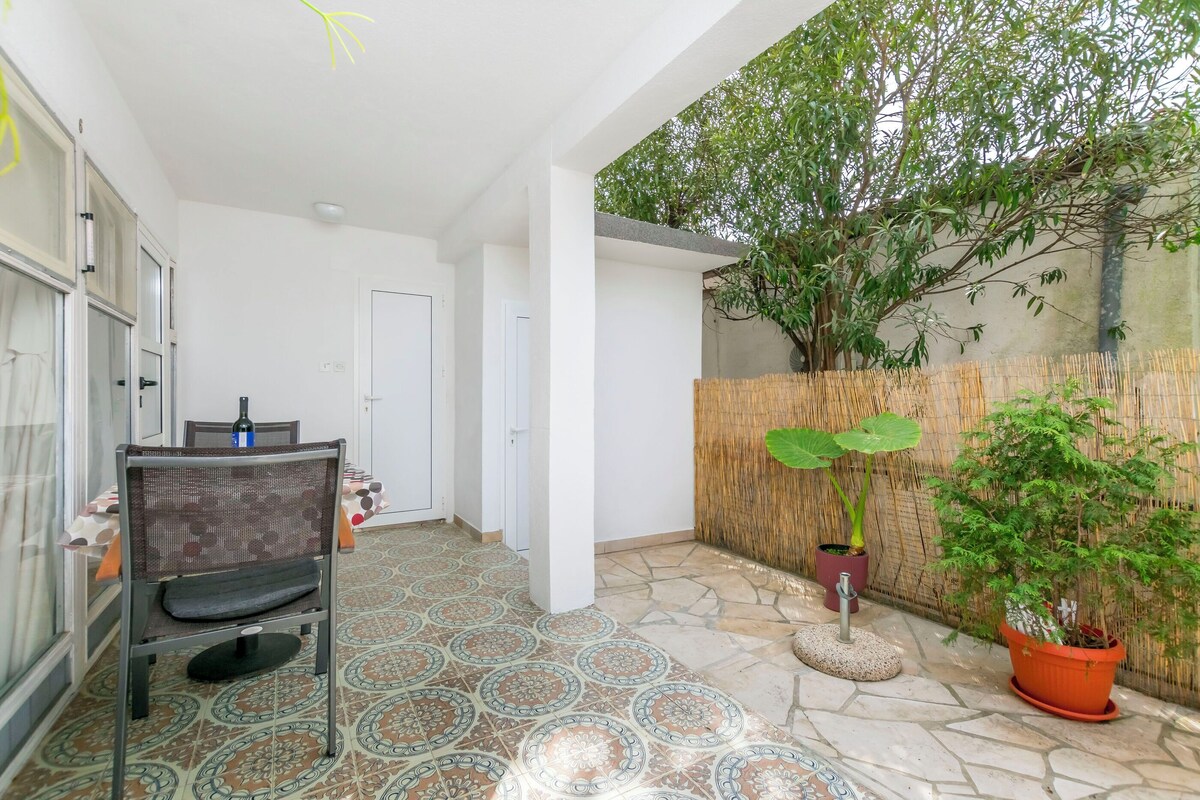 A patio area with a dining table, chairs, potted plants, and a stone-tiled floor.