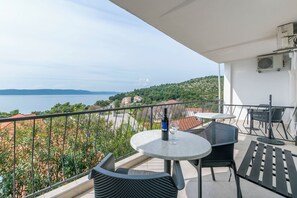 A balcony with a table and chairs, overlooking a body of water and greenery. - Apartments Blato Beach (Podgora)