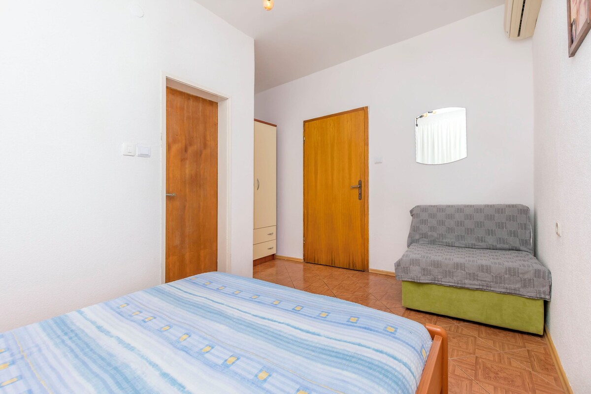 A bedroom with a bed, a green sofa, two wooden doors, and a window with blinds.