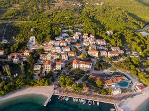An aerial view of a coastal resort with multiple buildings, a marina, and a beach. - Apartments Blato Beach (Podgora)