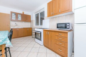 A kitchen with wooden cabinets, a microwave, an oven, and a window. - Apartments Blato Beach (Podgora)