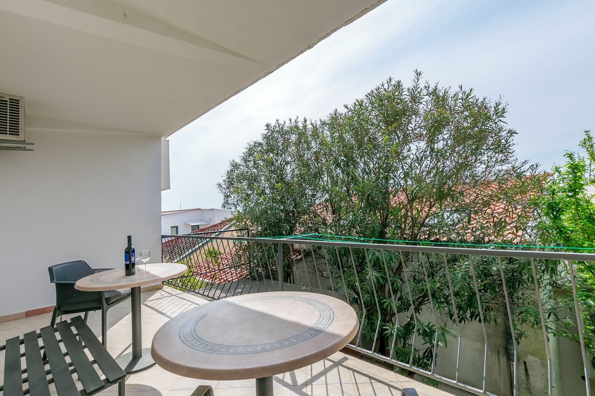 A balcony with two round tables, a chair, and a bottle of wine.