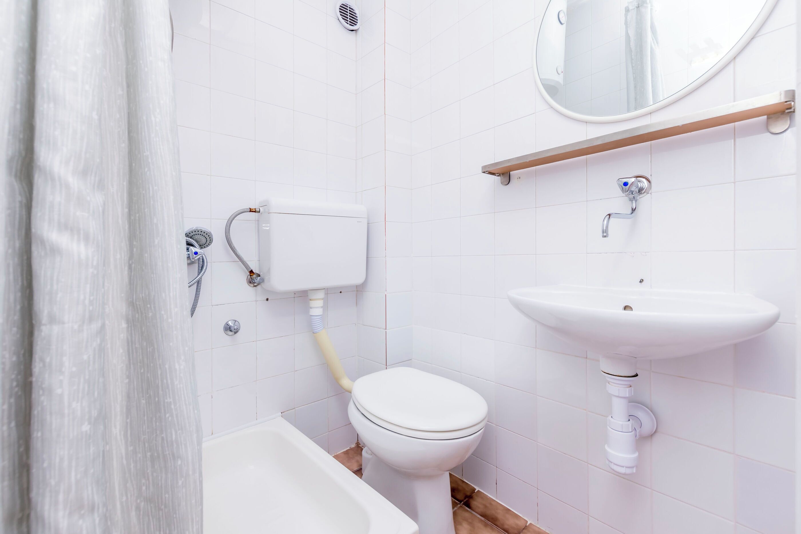 A bathroom with a toilet, sink, shower, and a mirror.