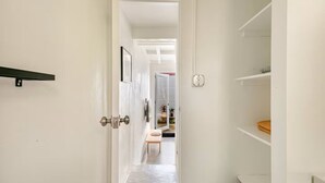 Um corredor com uma porta, uma mesinha e uma lixeira.