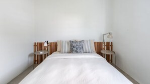 Quarto com cama, duas mesas de cabeceira, encosto e luminária na parede.