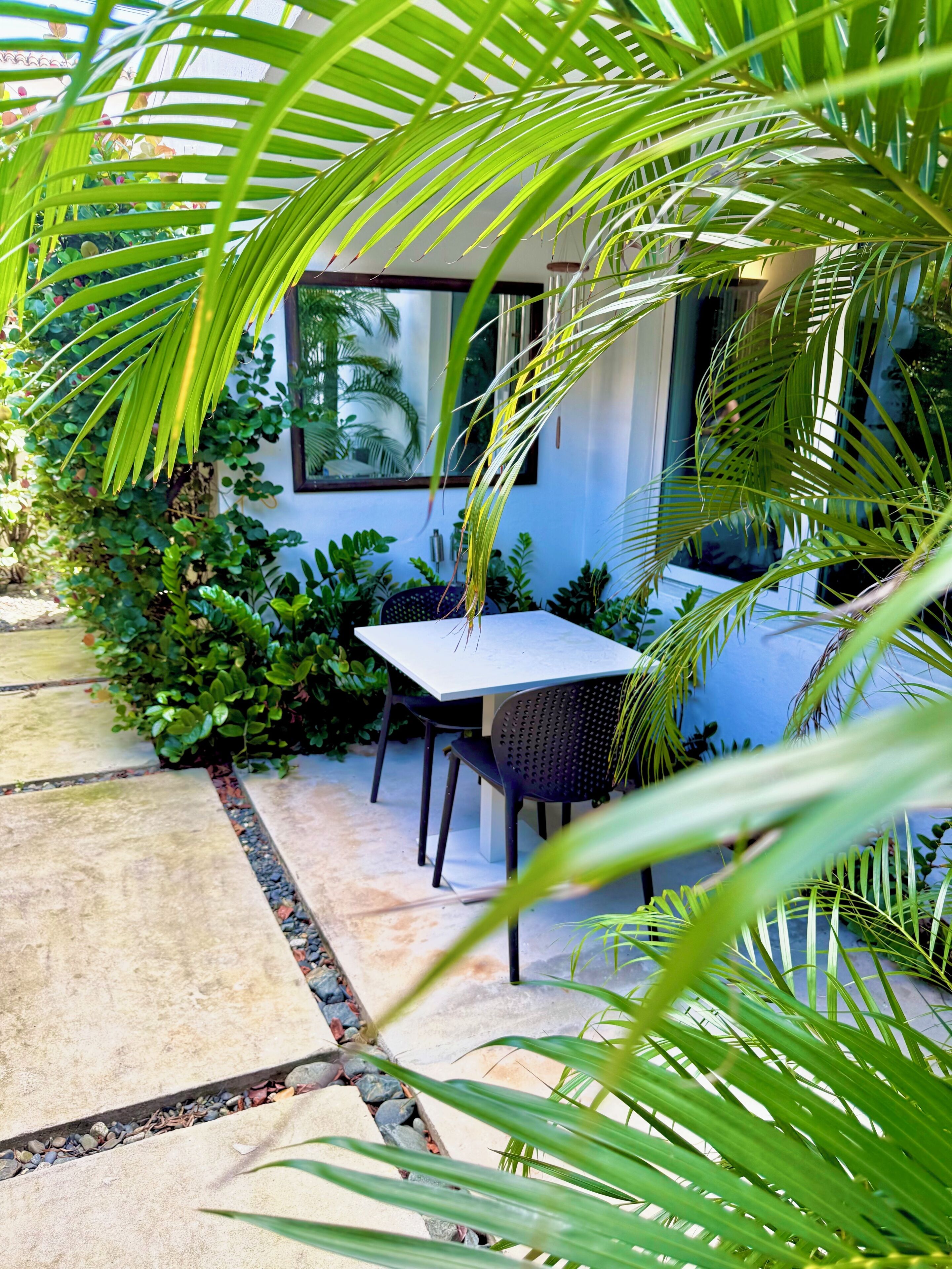 An outdoor seating area with a table and chairs, surrounded by lush greenery and a stone pathway.