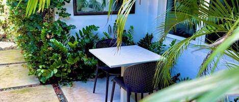 An outdoor seating area with a table and chairs, surrounded by lush greenery and a stone pathway.
