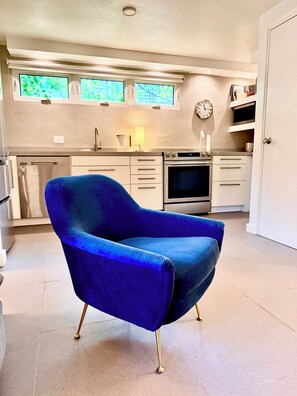 Una cocina moderna con un sillón azul, electrodomésticos de acero inoxidable y un reloj en la pared.
