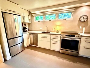A modern kitchen with stainless steel appliances, a dishwasher, a double oven, and a window with a view. - Monaco Garden-Level Urban Enclave by Stay Here PR (San Juan)