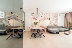 A modern living room with a dining area, a grey sofa, a coffee table, and a wall with floral artwork. - Villa Axi by old Town (Sibenik)