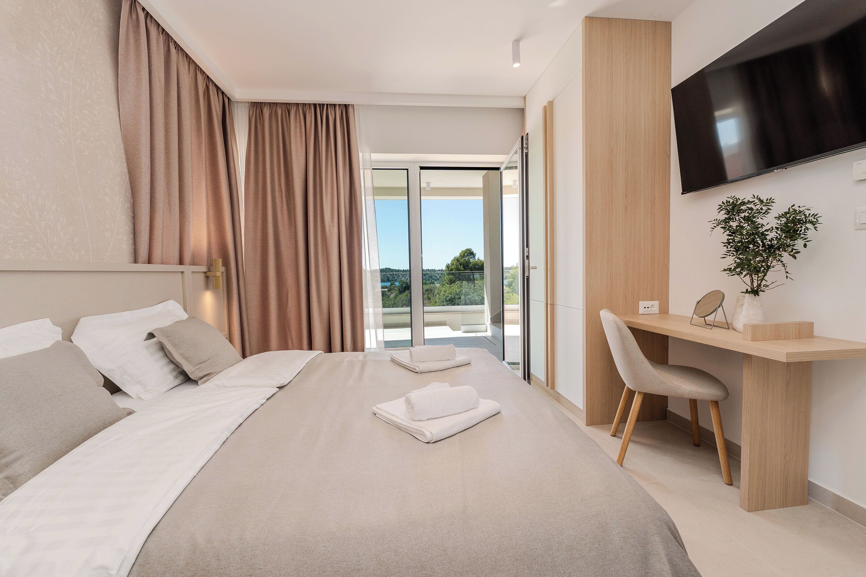 A modern hotel room with a bed, a desk, a chair, a TV, and a view of the outdoors.