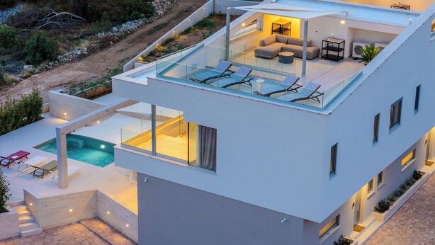 Een modern meerlaags huis met een terras op het dak, een zwembad en een goed verlicht interieur.