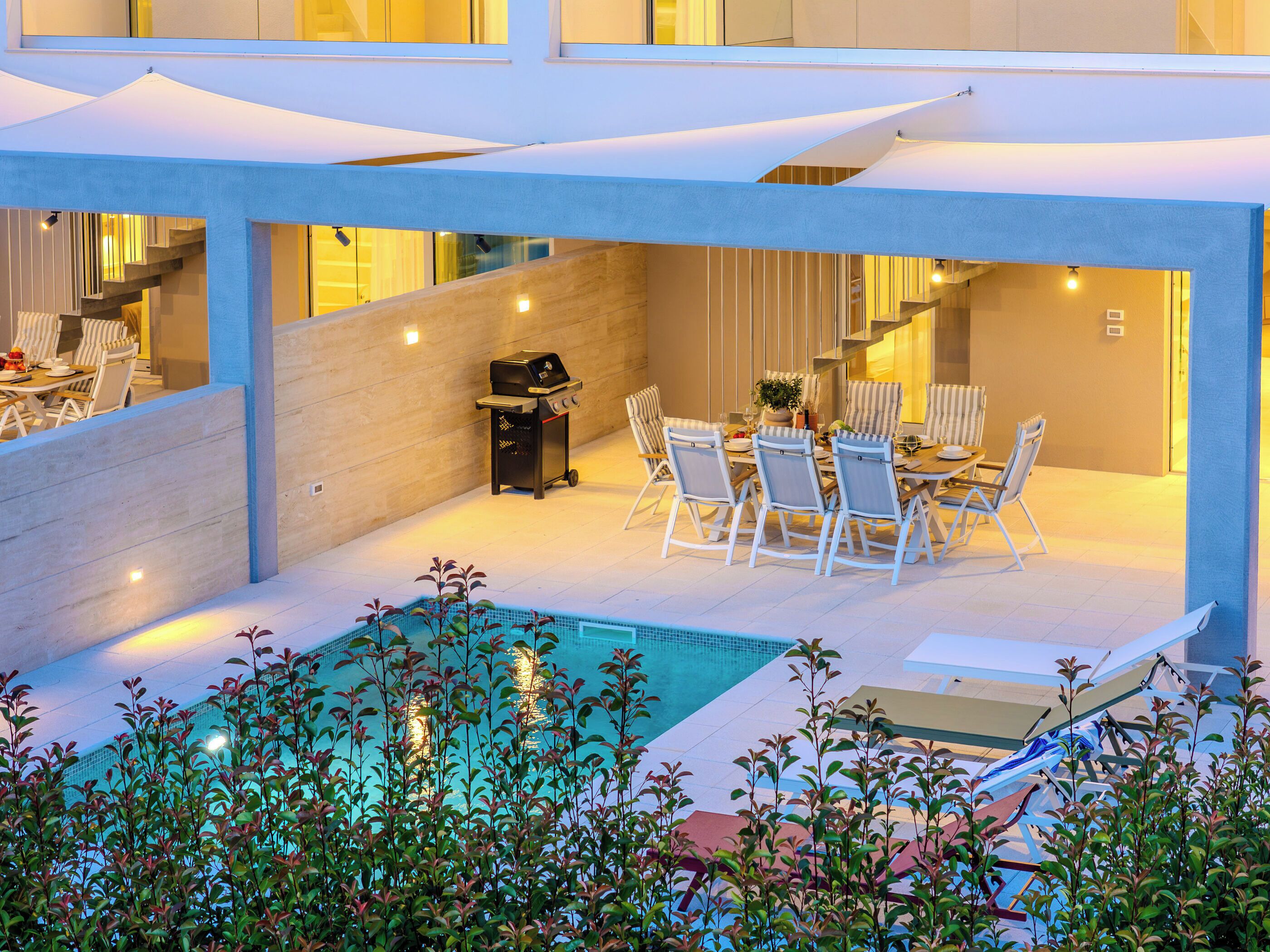 A modern outdoor dining area with a pool, a barbecue grill, and a staircase leading to an upper level.