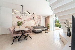 A modern living room with a dining area, a gray sofa, a coffee table, and a large abstract mural on the wall. - Villa Axi by old Town (Sibenik)