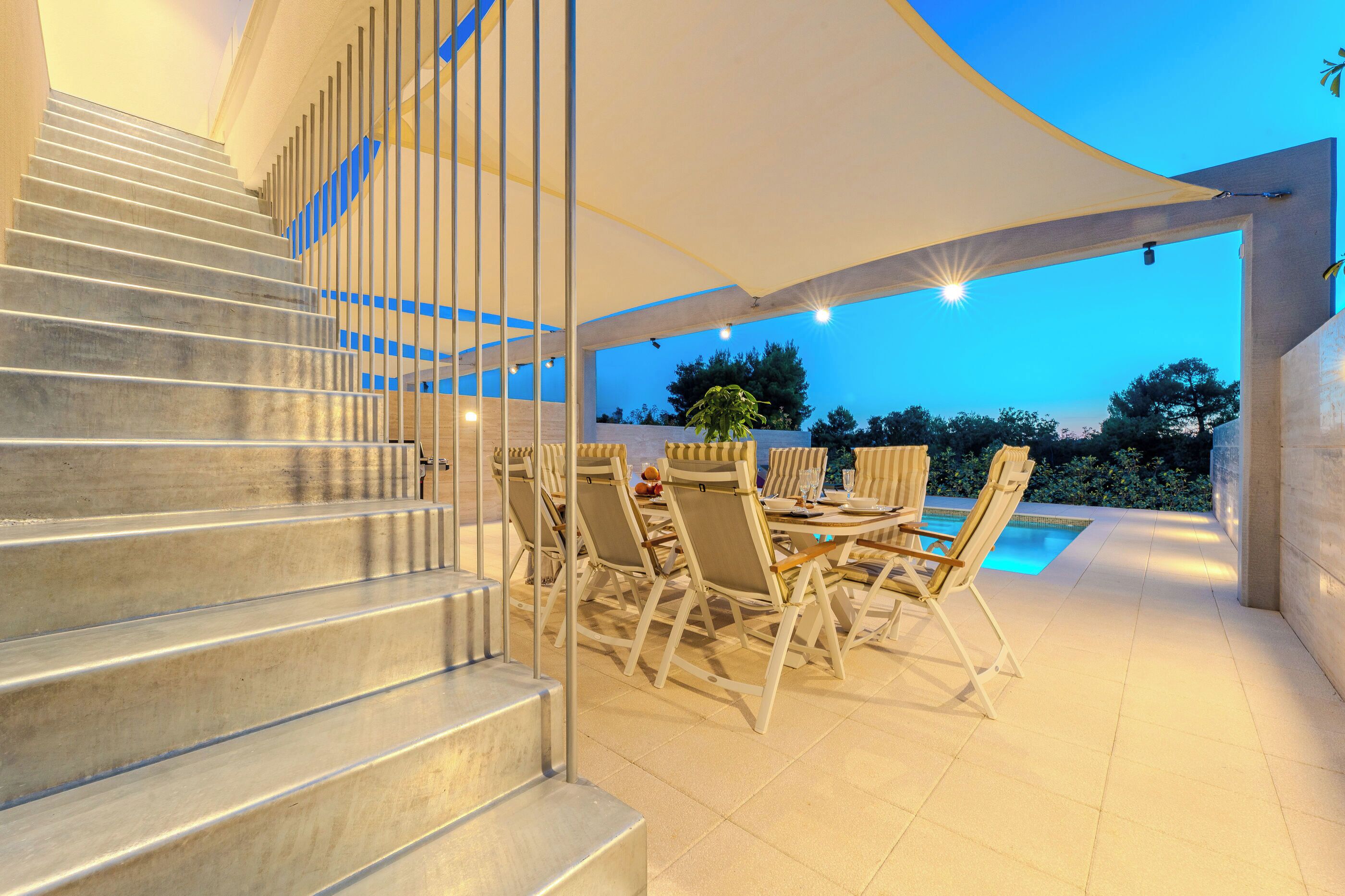 Une terrasse extérieure moderne, dotée d’une piscine, d’un escalier et de mobilier d’extérieur.