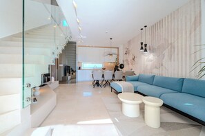 Ein modernes Wohnzimmer mit einem blauen Sofa, einer Glastreppe und einer Küche im Hintergrund.