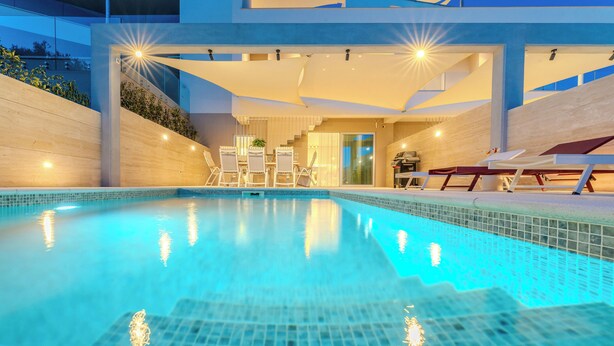A modern indoor swimming pool with clear blue water, surrounded by lounge chairs and a staircase leading to an upper level. - Villa Nexi by old Town (Sibenik)