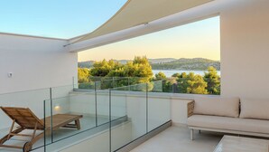A balcony with a glass railing, a wooden lounge chair, a sofa, and a view of a lake and trees. - Villa Nexi by old Town (Sibenik)