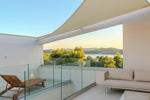 A balcony with a glass railing, a wooden lounge chair, a sofa, and a view of a lake and trees. - Villa Nexi by old Town (Sibenik)