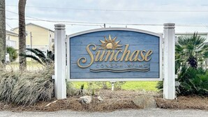Une enseigne pour le complexe de copropriétés Sunchase, ornée d’un symbole solaire, et entourée d’espaces verts aménagés et d’immeubles résidentiels.