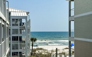 Un hotel frente a la playa con varios balcones, una playa de arena y el océano al fondo.