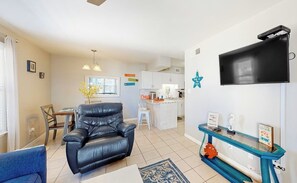 Ein Wohnzimmer mit einem schwarzen Ledersessel, einem blauen Sofa, einem Glastisch und einem an der Wand befestigten Fernseher.
