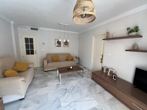 Ein Wohnzimmer mit Sofa, Couchtisch, Fernseher und einer Pendelleuchte.