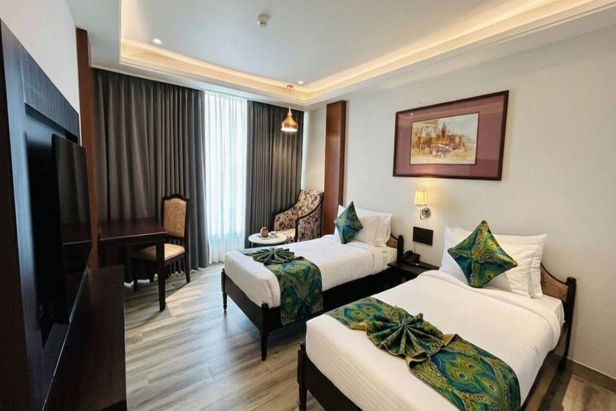 Ein Hotelzimmer mit zwei Betten, einem Schreibtisch, einem Sessel, einem Fernseher und einem Bild an der Wand.