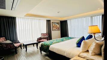 A hotel room with a bed, a desk, a chair, a sofa, and a window with curtains.