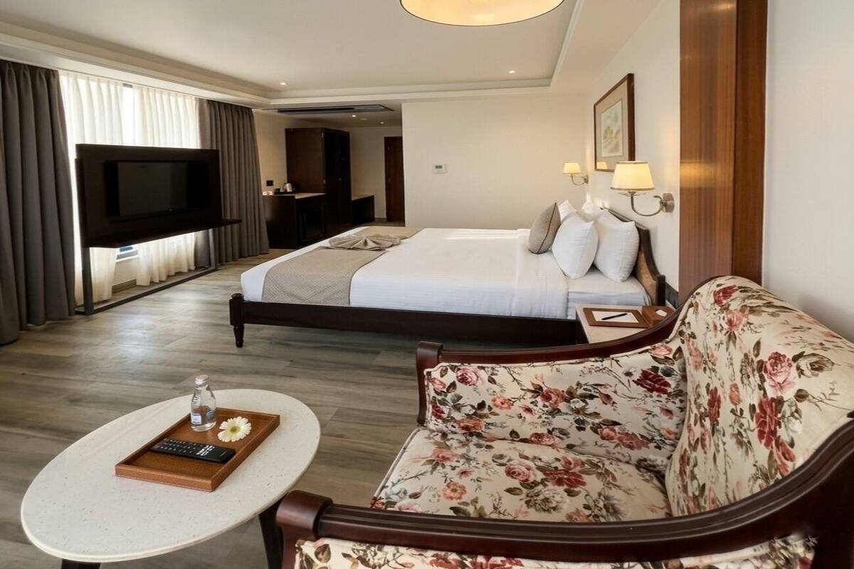 Ein Hotelzimmer mit einem Bett, einem Sofa, einem an der Wand befestigten Fernseher, einem Nachttisch mit Tablett und einer Pendelleuchte.