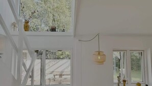 Ein Zimmer mit hohen Decken, großen Fenstern, einer Pendelleuchte und einer Treppe.