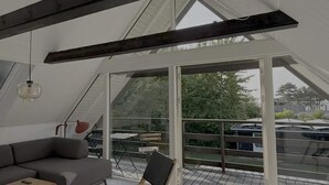 Ein modernes Schlafzimmer im Loft-Stil mit einem großen Dachfenster, einem grauen Sofa, einem Holzstuhl und einem kleinen Tisch.