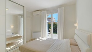 Un dormitorio con cama, espejo, aire acondicionado y vistas al exterior.