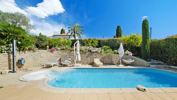 Piscina con sillones de descanso, muro de piedra y diversas plantas y árboles.
