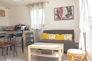 Un espace de vie comprenant un canapé, des fauteuils, une table, un coin cuisine avec un four à micro-ondes et une fenêtre avec des rideaux.