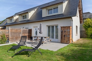 A two-story house with a patio area featuring a table and two lounge chairs. - 2-Star Holiday Home “L'Austreberthe des Abbayes du Val de Seine” (Sainte-Marguerite-sur-Duclair)