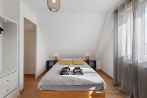 Une chambre avec un plafond en pente, un lit recouvert d’une couvre-lit à motifs floraux, deux lampes de chevet, une armoire et un luminaire suspendu.
